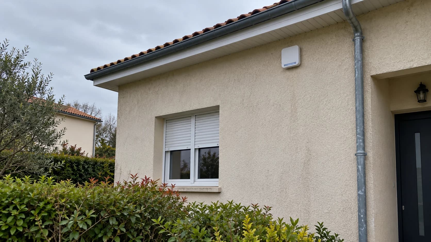 Sirène d’alarme fixée en hauteur sur la façade d’une maison, sous une avancée de toiture